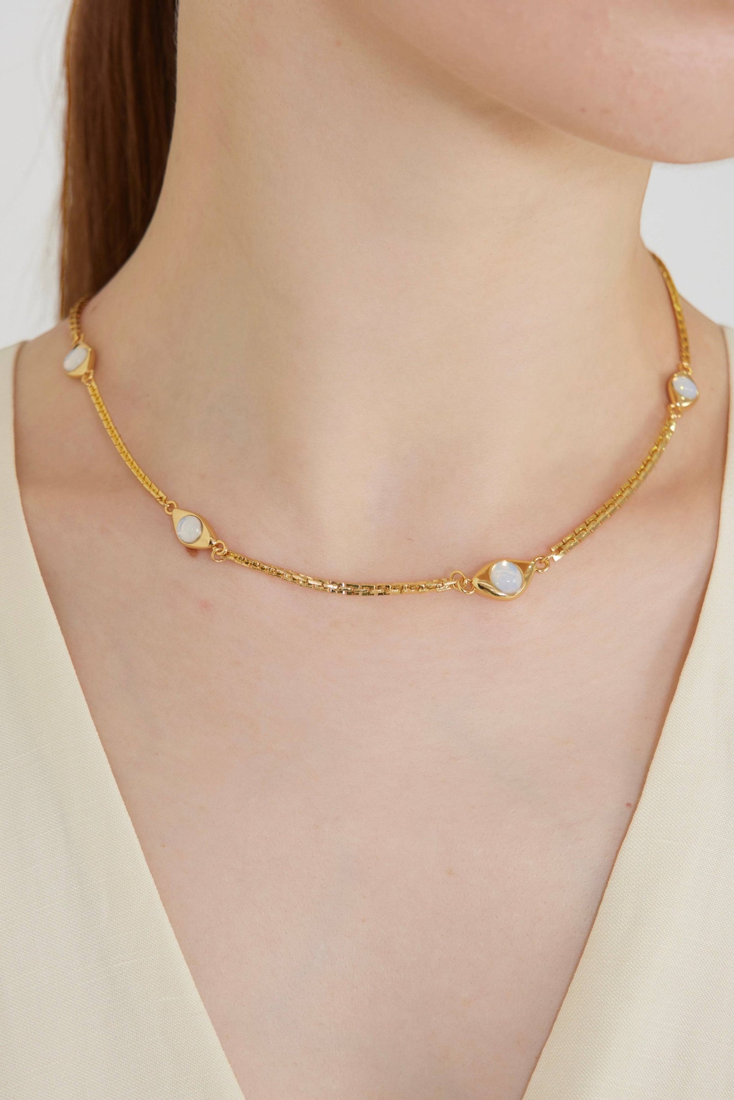a woman wearing a gold necklace with white stones